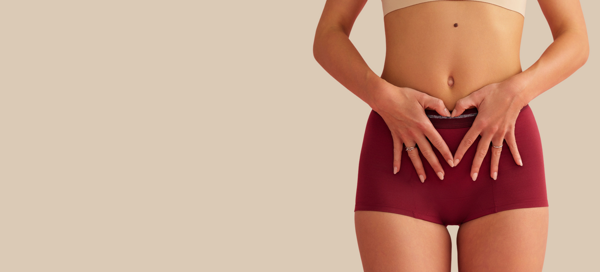 Ausschnitt eines Models, das eine rote Perioden-Shorts von ooia trägt und ein Herz mit ihren Händen auf ihrem Unterbauch formt.