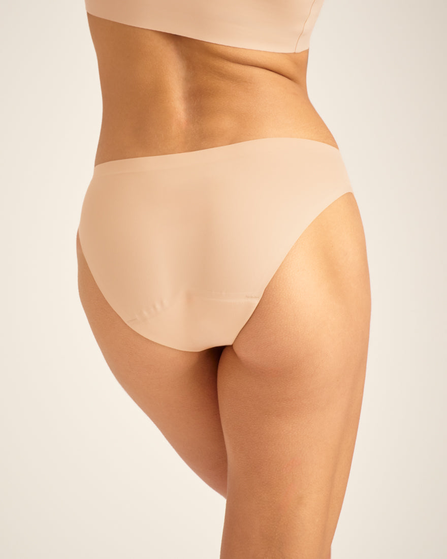 Modell trägt ooia Slip Seamless in Beige – nahtlose Periodenunterwäsche im klassischen Schnitt. Rückansicht.
