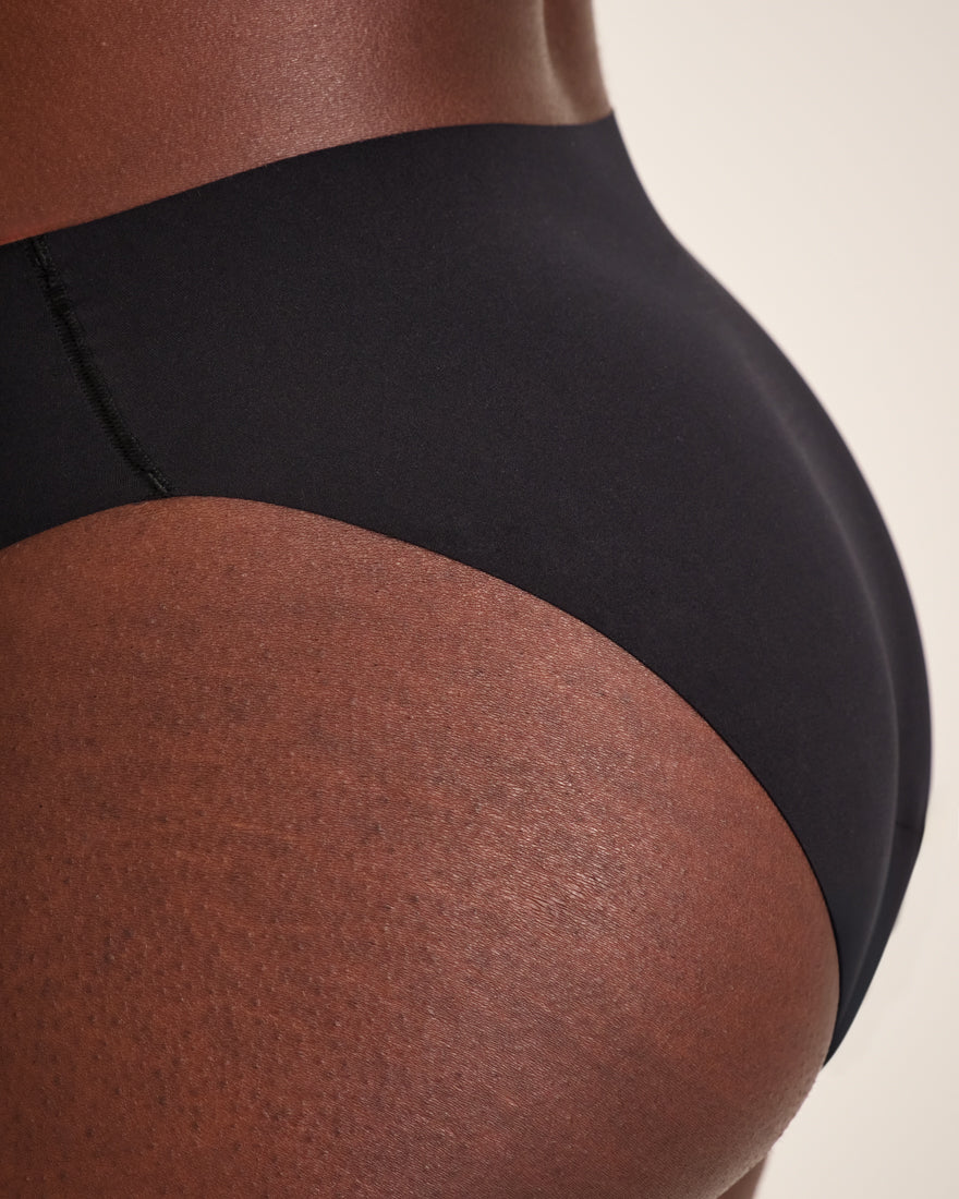 Modell trägt ooia Slip Seamless in Schwarz – nahtlose Periodenunterwäsche im klassischen Schnitt. Detailansicht.