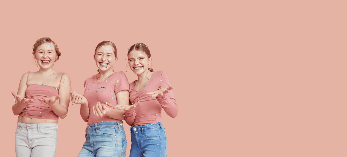 Drei Teenager Mädchen lachen und werfen Konfetti hoch.