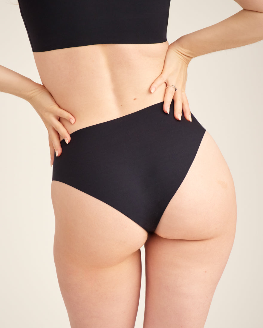 Modell trägt ooia everyday Slip Seamless in Schwarz – nahtlose Unterwäsche, die Slipeinlagen ersetzt. Rückansicht.