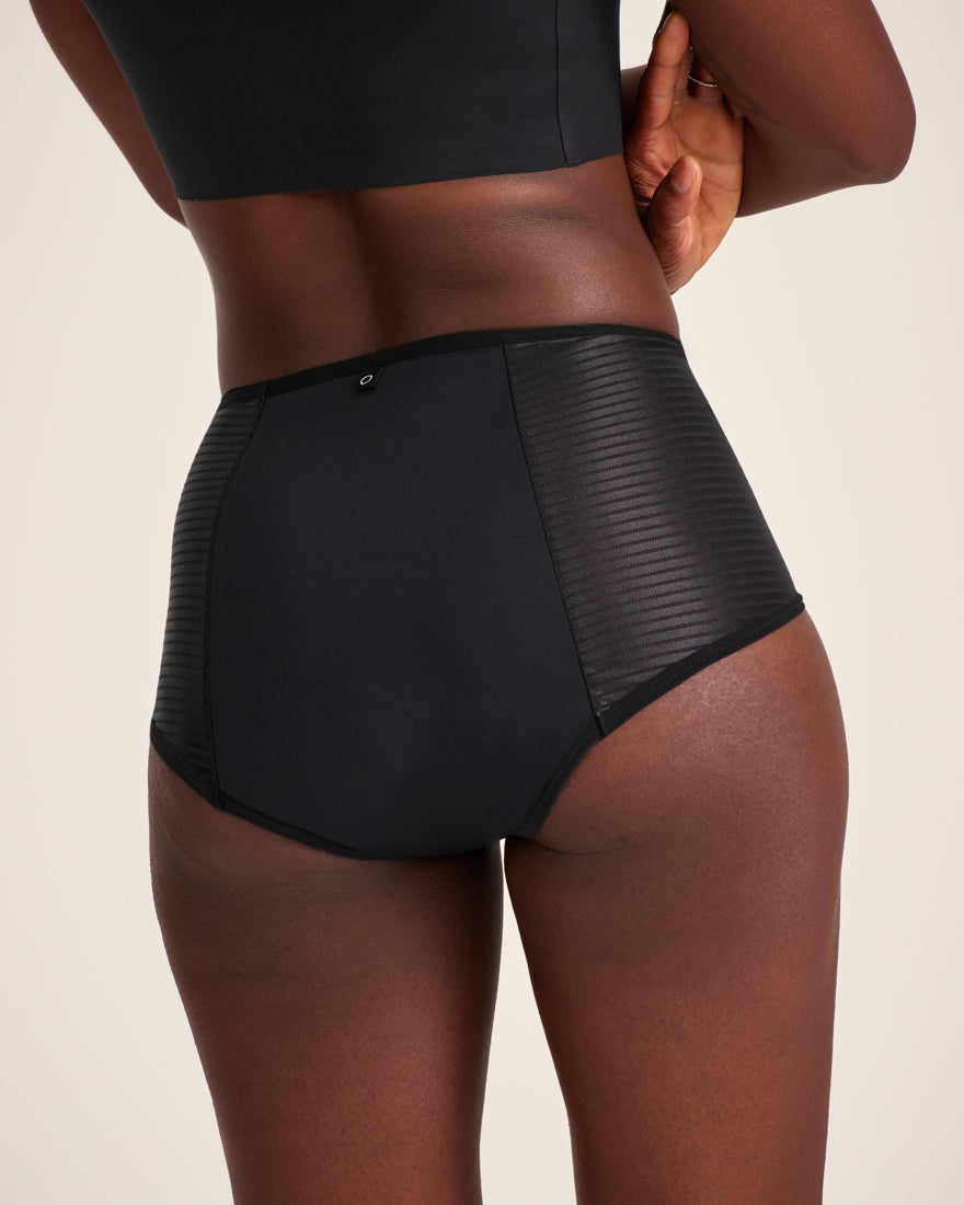 Modell trägt ooia Highwaist Extra Strong in Schwarz – Periodenunterwäsche mit hohem Bund und Glanzdetail. Rückansicht.