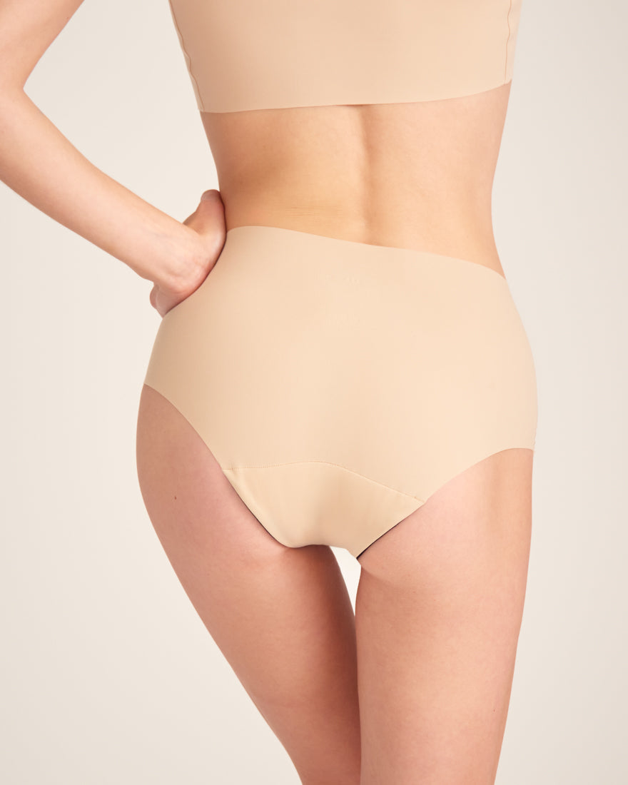 Modell trägt ooia Highwaist Seamless in Beige – nahtlose Periodenunterwäsche mit hohem Bund. Rückansicht.