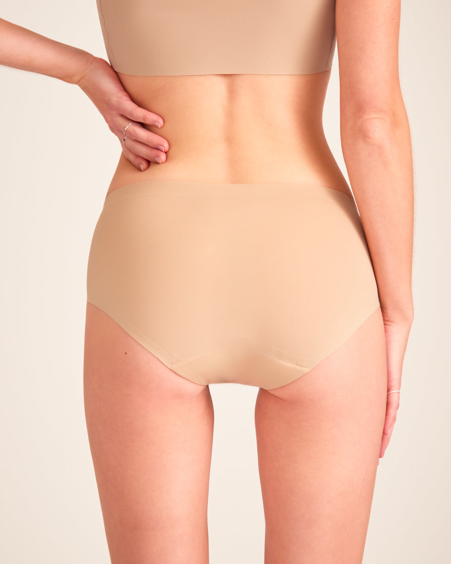Modell trägt ooia Hipster Seamless in Beige – nahtlose Periodenunterwäsche. Rückansicht.