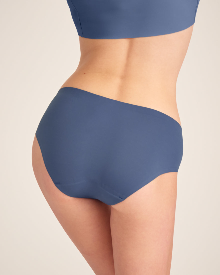 Modell trägt ooia Hipster Seamless in Smoky Blue – nahtlose Periodenunterwäsche. Rückansicht.