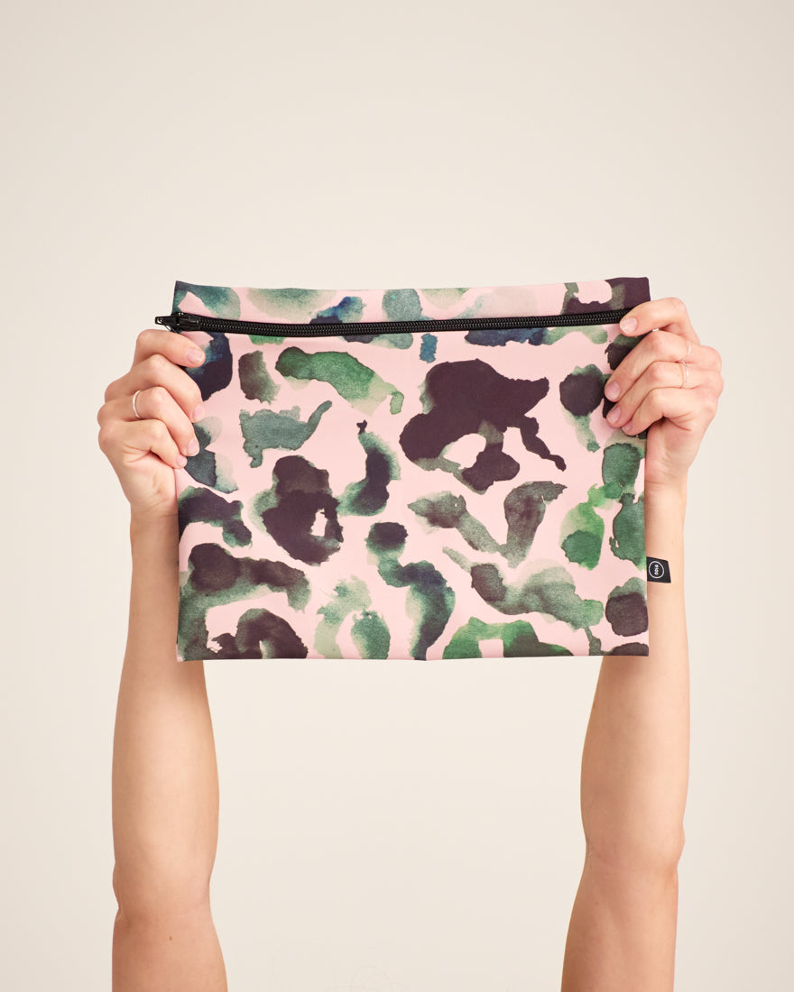 Modell hält die ooia Wetbag Maxi, in großem Design, mit rosa-grün-schwarzem Aufdruck und flüssigkeitsundurchlässigem Innenstoff.
