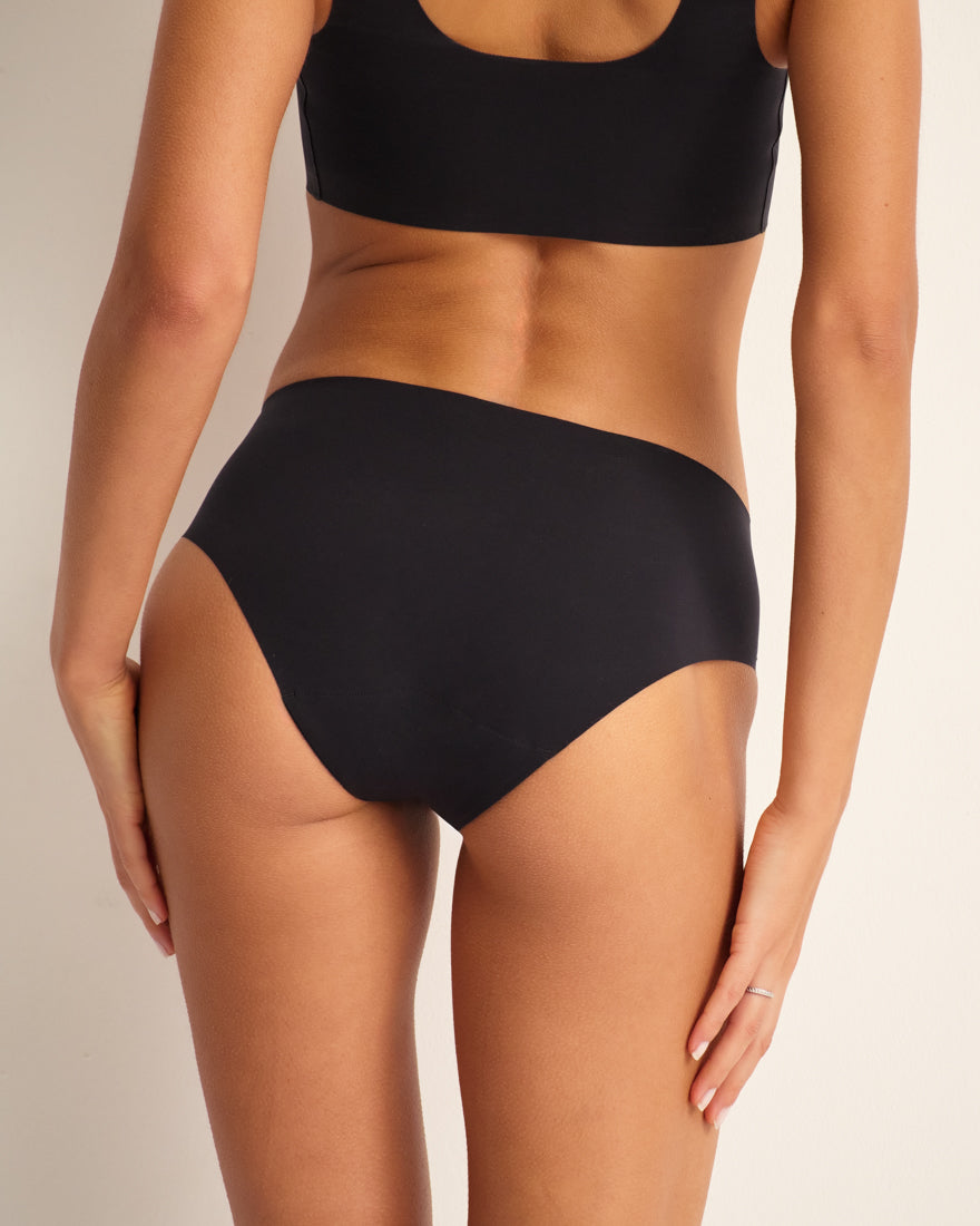 Modell trägt ooia Hipster Seamless in Schwarz – nahtlose Periodenunterwäsche. Rückansicht.