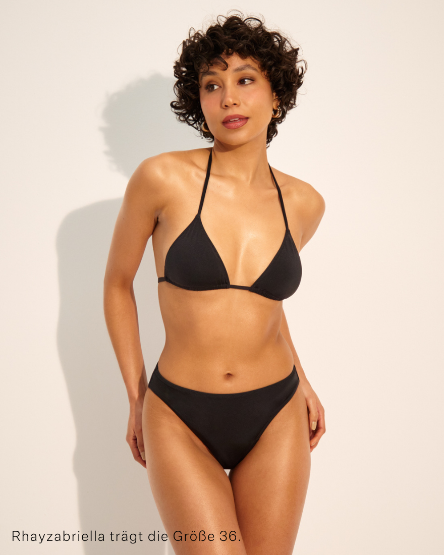 Model trägt ooia Perioden Bademode Slip in schwarz.
Frontal stehend